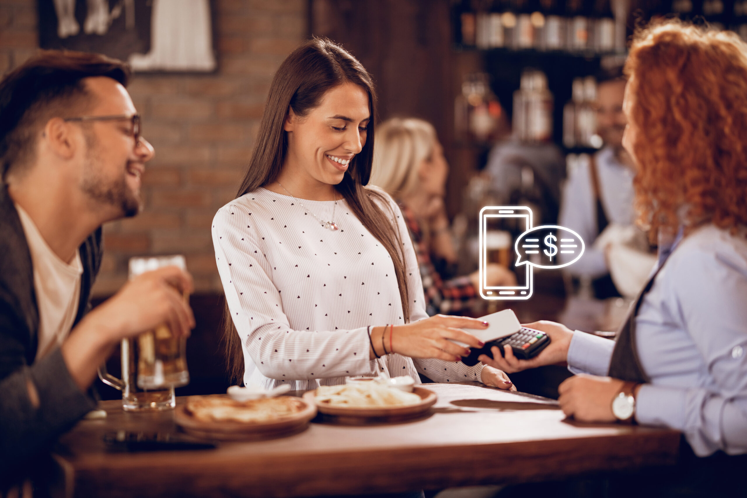 Young happy woman using smart phone while paying for a bill to a waitress in a bar.